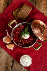Freshly cooked homemade russian famous soup borsch. Served in cooper pan with garlic, sour cream and dill. Nourishing tasty meal. Rustic style, close up, wooden background, flat lay, top view