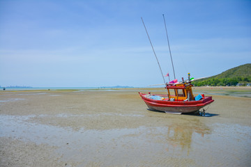 Fototapeta premium Fishing boat parked on the beach,Fishing boat parked on the seashore,Small fishing boat parked and moored on the beach at low tide. Boat and anchor at the beach in summer vacation. Sunny day.
