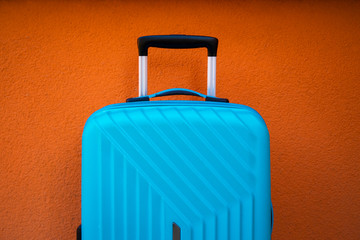 Turquoise travel bag on orange wall background; travel and object concept.