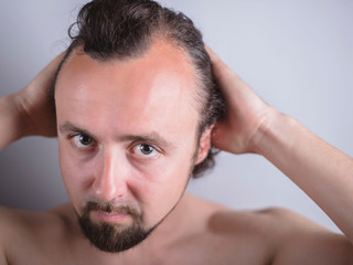 Portrait of a young guy with magnificent hair that falls early on his forehead. The problem of premature aging. Combing hair and indignantly looking in the mirror