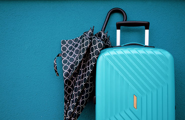 Turquoise travel bag and an umbrella on blue wall background; travel and object concept.