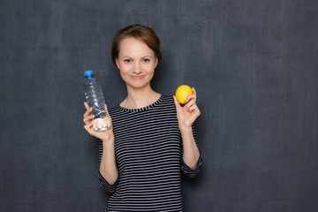 Portrait of happy girl holding lemon and bottle of water and smiling