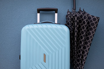 Blue travel bag and an umbrella on blue wall background; travel and object concept.