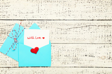 Blue paper envelopes with red heart and text With Love on white wooden table