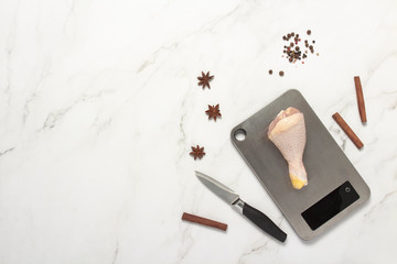 Chicken leg on the scales knife and spices on the marble table. Cooking concept. Flat lay top view