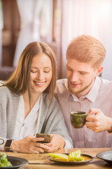 couple in a cafe smiling looking at the phone