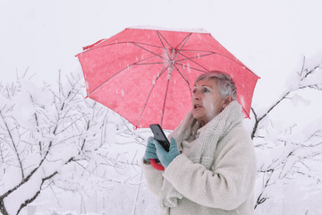 older woman with red umbrella in the snow talking on mobile phone