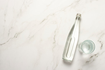 Glass bottle of water and a glass of water on a marble table. The concept of heat, water balance, diet, weight loss, refreshing drinks. Flat lay, top view