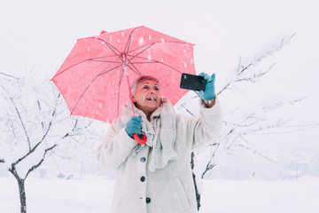 older woman with red umbrella taking a picture with lots of snow 