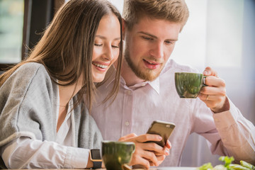 couple in a cafe smiling looking at the phone
