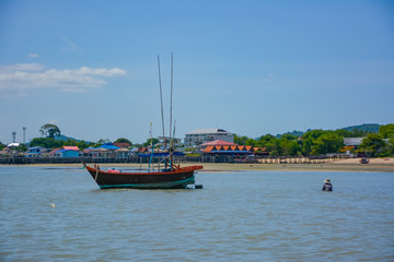 Fototapeta premium Fishing boat parked on the beach,Fishing boat parked on the seashore,Small fishing boat parked and moored on the beach at low tide. Boat and anchor at the beach in summer vacation. Sunny day.