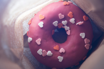Pink donut with hearts in a paper bag, closeup. top view