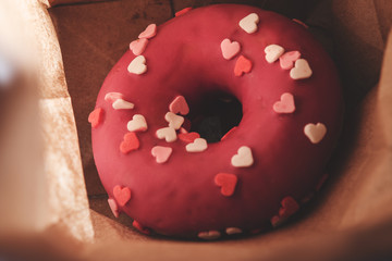 Pink donut with hearts in a paper bag, closeup. top view