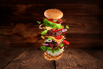 Maxi hamburger, double cheeseburger with flying ingredients isolated on wooden background. High resolution image