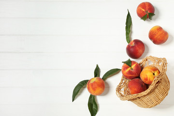Fresh peaches with green leafs in basket on white wooden table