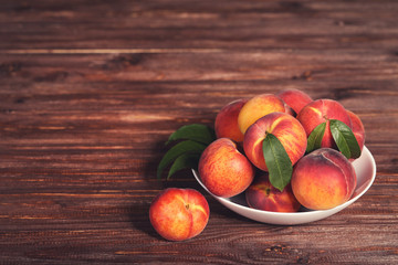 Fresh peaches with green leafs in plate on brown wooden table