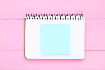 Blank notepad with paper sticky note on pink wooden table