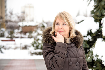 Portrait of happy mature woman in snowy park on winter vacation. Сlose up рortrait of a mature woman in winter