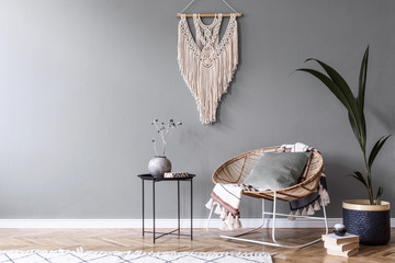 Modern boho interior design of sitting room with design rattan armchair,coffee table, beige macrame, tropical plants and elegant accessories. Stylish home decor.  Template. Copy space. Home staging.