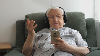 Old woman is listening music (old hits) on a smartphone.