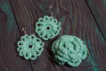 Homemade knitted earrings and brooch in light green color. On brushed pine boards painted in black and green.