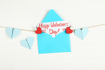 Paper envelope with hearts and text Happy Valentines Day hanging on white wooden background