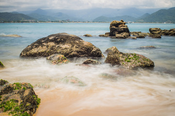 Fototapeta na wymiar Waves long exposure, Ubatuba, Sao Paulo, Brazil - Paradise tropical beach with white sand, blue and calm waters, without people on a sunny day and blue sky of the Brazilian coast in high resolution