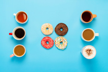 Tasty donuts and cups with hot drinks on a blue background. Concept of sweets, bakery, pastries, coffee shop, friends, friendly team. Flat lay, top view