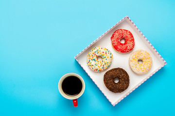 Tasty donuts in a box and a cup with hot coffee on a blue background. Concept of sweets, bakery, pastries, coffee shop. Square. Flat lay, top view