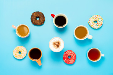 Obraz na płótnie Canvas Tasty donuts and cups with hot drinks, coffee, cappuccino, tea on a blue background. Concept of sweets, bakery, pastries, coffee shop, meeting, friends, friendly team. Flat lay, top view