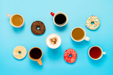 Obraz na płótnie Canvas Tasty donuts and cups with hot drinks, coffee, cappuccino, tea on a blue background. Concept of sweets, bakery, pastries, coffee shop, meeting, friends, friendly team. Flat lay, top view
