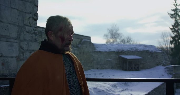 Old, wounded hetman in armor with sword walks at fortress and looks around