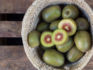 kiwis rojos enteros y partidos  en cesta de mimbre sobre madera