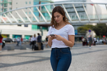 Beautiful young woman walking on street with phone. Low angle view of attractive peaceful brunette using smartphone. Technology concept