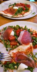 View from above on 2 Pizza with ham, tomatoe, mozzarella and arugula salad on a white plate