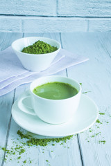 A Cup of traditional green Japanese matcha tea on a white wooden table against a brick wall