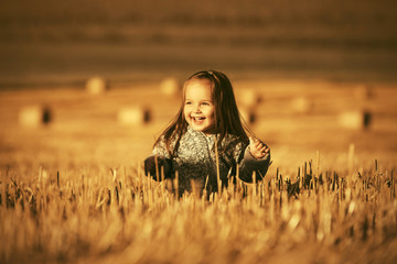Happy two year old girl walking in summer harvested field