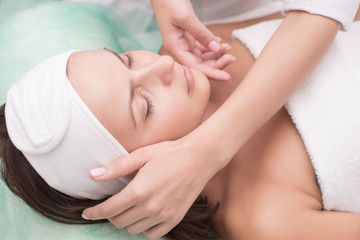 Girl massage therapist does facial massage with a beautiful woman. Hands are closing. Massage room