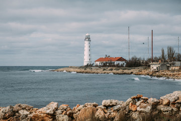 Colorful seascape with a white lighthouse on a rocky coast at Cape Chersonese against a cloudy sky