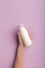 Hand holding bottle with coconut milk over purple background