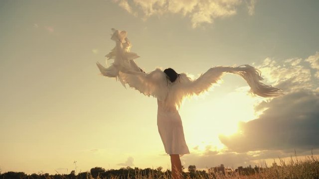 White angel and sun. Brunette girl in a white dress raises angel wings up, looks at the sunset