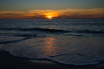 Obraz premium Wellen und Meer mit romantischen Sonnenuntergang und brennenden atemberaubenden Himmel am Horizont 