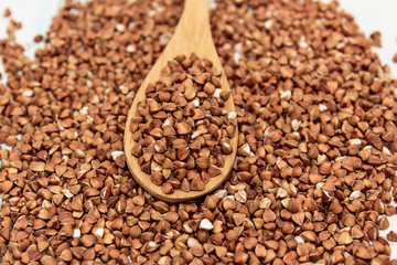 Buckwheat groats in a wooden spoon on a white wooden background. The concept of healthy nutrition and diet. Zero wast. Close-up.