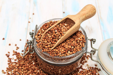 Buckwheat groats in a wooden spoon on a white wooden background. The concept of healthy nutrition and diet. Zero wast. Close-up.