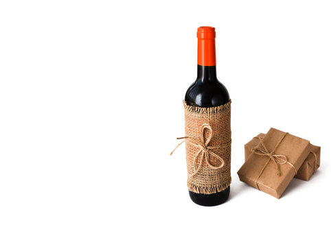 Bottle Of Red Wine Wrapped In Burlap Tied With Twine And Gift Boxes In Kraft Paper On White Background. Holidays Concept. Ideas Of DIY Gift Wrapping. Close-up. Copy Space