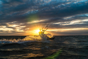 Silhouette of kitesurfer riding at the ocean in beautiful sunset condition with sun star and lens flare