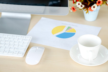 Business and workplace concept. Cup of hot coffee on work desk with computer keyboard and papers graphs