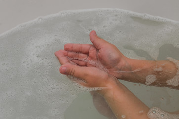 Fototapeta premium Hands of a child in soapy foam in the water while bathing in the bathroom