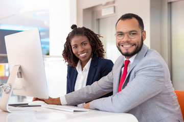 Cheerful business people using desktop computer. Young African American business people working with computer and smiling at camera in office. Business and technology concept