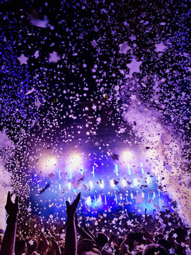 Menschen feiern vor einer B&uuml;hne auf einem Musikfestival mit Konfetti und bunten Scheinwerfern